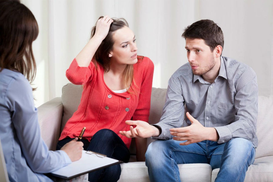 A woman and man sitting on the couch talking to another person.